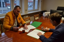 dwoch mezczyzn siedzacych przy stole i podpisujacych dokumenty