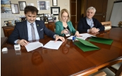 Trzy osoby siedzace przy stole i podpisujace dokumenty