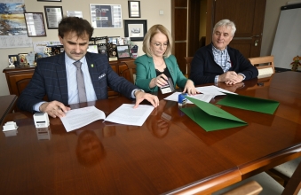 Trzy osoby siedzace przy stole i podpisujace dokumenty