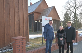 trzy stojace osoby w tle drewniany kosciol