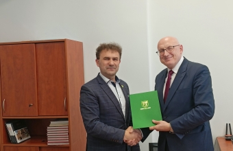 dwoch mezczyzn podaja sobie rece i trzymaja zielona teczke