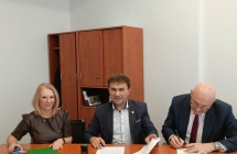 trzy osoby siedzace przy stole, jedna z osob podpisuje  dokumenty