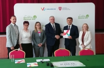 grupa stojacych osob, na pierwszym planie stol z zielonym nakryciem